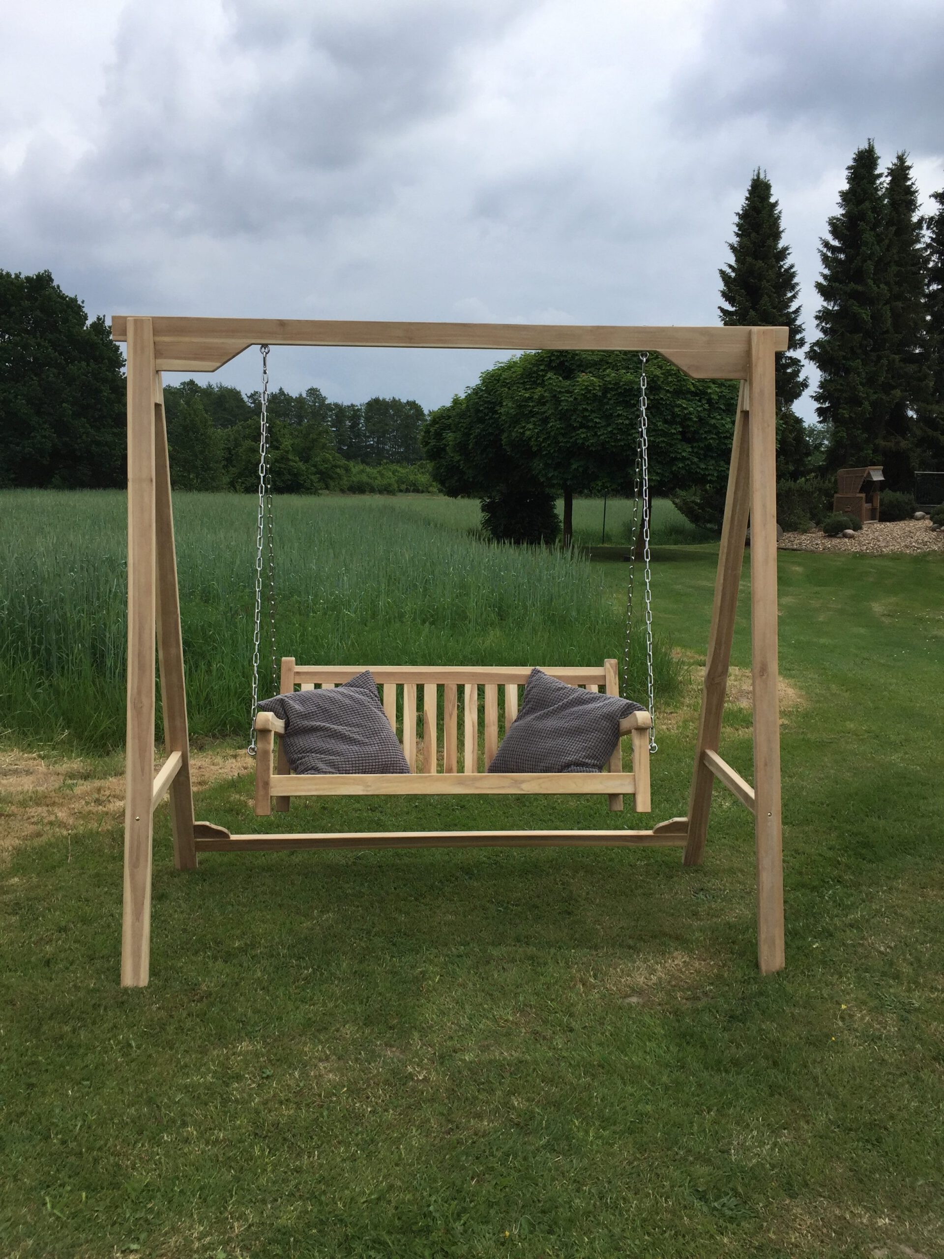 Schaukelbank Florenz aus Teakholz im Garten mit zwei Kissen