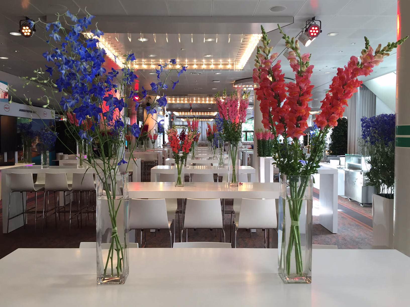 Floristikbeispiel Dinnertische an weißen Eventtischen mit hohen bunten Blumenvasen